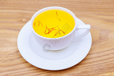藏红花在木本底的白色杯子里喝茶 来自红面纱的茶背景图片