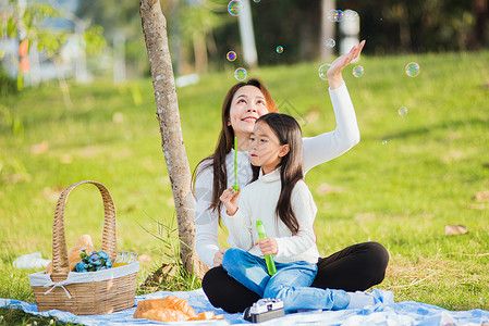 泡泡与女孩在野餐期间玩得开心 吹肥皂泡泡泡喜悦父母花园童年太阳女孩公园乐趣女士女儿背景