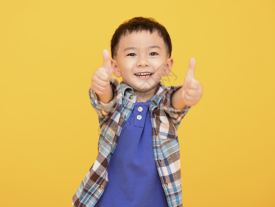 快乐的小男孩 在黄色背景面前 和显示拇指举起图片