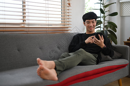 快乐的男人穿着温暖的毛衣在沙发上放松 使用智能电话 享受舒适的家休闲周末时间背景图片