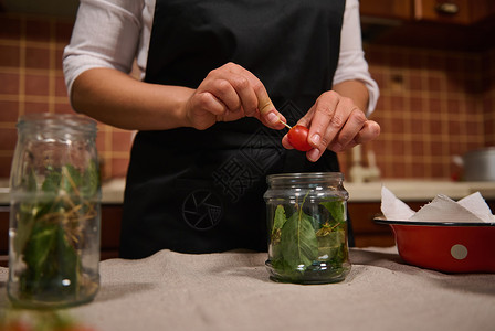 根据传统家庭食谱 黑厨围裙内主妇在家中厨房里用樱桃番茄做樱红菜背景图片