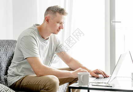 英俊的年轻人在笔记本电脑上工作白色枕头网络远程男人男性客厅公寓沙发工作者远程工作者高清图片素材