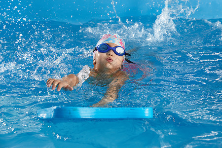 小女孩学会游泳 在室内游泳池与游泳池板女孩运动班级婴儿游泳者木板练习学校活动风镜背景图片