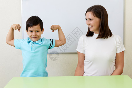 男孩正向老师展示他的手臂肌肉冒充二头肌拳头男性运动女士力量微笑孩子童年背景图片