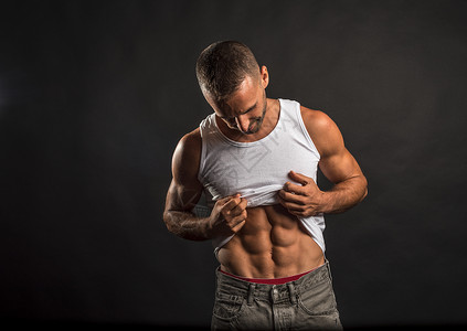 运动健壮的人抬起衬衫露出腹部工作室运动员背心优势男性肌肉黑色腹肌背景图片