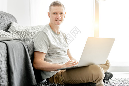 英俊的年轻人在笔记本电脑上工作枕头客厅自由职业者商业公寓沙发键盘互联网工作者成人男人高清图片素材