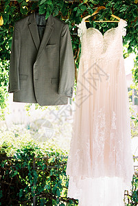 新娘礼服和新郎外套挂在树下花园的衣架上背景图片