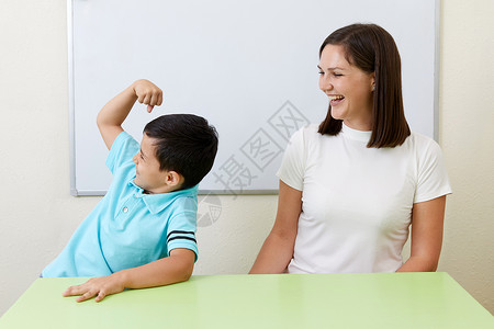 男孩正向老师展示他的手臂肌肉力量二头肌孩子男性女士冒充身体运动微笑拳头背景图片