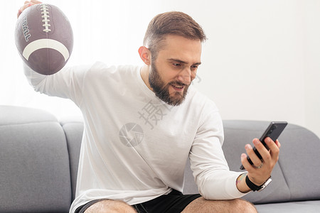 足球手素材美国足球球迷拿着橄榄球 在智能手机上看比赛和比赛客厅锦标赛职业枕头格子扇子设备电话胡子数字背景