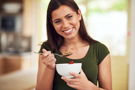 吃啥补啥吃啥变啥 一个快乐的年轻女人站在她的厨房里吃一碗牛奶什锦早餐的画像背景