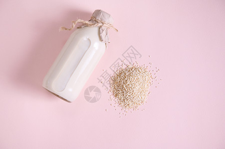 粉红色表面上的一堆白米和一瓶基于植物的有机健康米浆 素食有益健康的不含乳制品的饮料背景