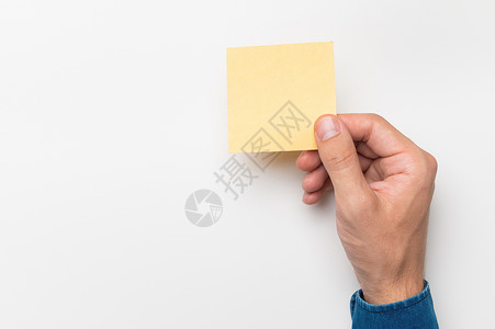 白色贴纸一个穿着牛仔衬衫的男人的手拿着一张文具贴纸 用于在白色背景上书写 空白纸空白提醒待办事项列表 办公用品注释消息 办公室和商业概念背景