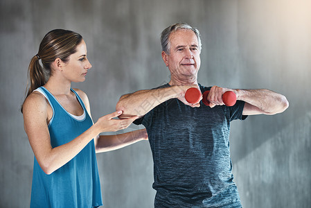 承诺在任何年龄都保持活跃和强壮 一名老年男子 在理疗师的帮助下使用重量表背景图片