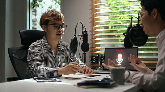 年轻人电台主持人在工作室录制现场播客时在工作室采访客人 广播 播客 博客和技术概念背景图片