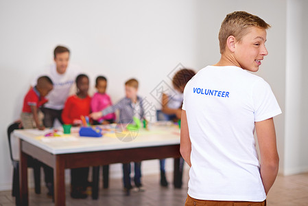 志愿者是社区的中坚力量 一名志愿者的后视照片 他正在观看其他志愿者在后台与小孩一起工作背景