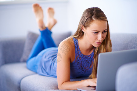 一位年轻女性在家沙发上使用笔记本电脑 她写了一封邮件背景图片