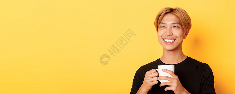 笑得开心的金发亚洲帅哥的特写 一边喝着咖啡 一边带着梦幻般的怀旧表情 站在黄色背景上广告员工潮人男性职业头发成人教育快乐理发背景图片