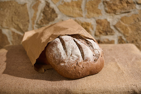 仍然活着 手工艺的全谷物健康小麦面包在桌上一个可回收纸袋里 上面装有布布桌布背景图片