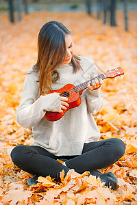 枫叶吉他素材Ukulele用女人的手握着Ukulele 在秋天户外演奏一个音响乐器背景