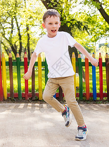 一个穿着白色T恤衫的快乐男孩 正在公园里跳舞呢背景图片
