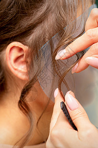近身发型设计师给美容院的年轻女子做发型造型职业后台黑发手指卷曲造型师女孩头发顾客背景图片