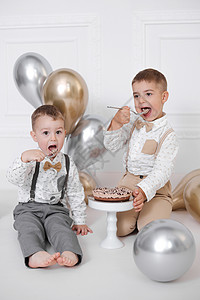 两个男孩庆祝生日 孩子们有一个 B 日派对 用蜡烛和气球的生日蛋糕 快乐的孩子们吃蛋糕 庆祝 白色简约的内饰喜悦工作室极简甜点金背景图片
