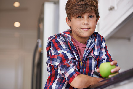 期盼着吃这个脆薄的绿苹果 一个小男孩靠厨房柜台向上倾斜青年烹饪微笑黑发男生男性孩子房子青少年水果背景图片