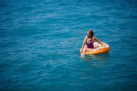 漂浮在透明绿松石海中的充气大甜甜圈上的年轻女子 一位苗条的女士在土耳其 埃及 地中海度假时放松身心戒指假期太阳晴天旅行天线游泳派背景图片