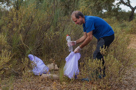 男人靠着垃圾袋 在废山上打扫垃圾袋气候主义者回收手套瓶子垃圾清理精神塑料生态背景图片