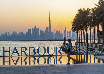阿联酋迪拜  09 18 2021 年轻女孩欣赏迪拜天际线的景色 从迪拜河港拍摄 户外建筑学天空旅行城市码头地平线全景记录阴霾景背景图片