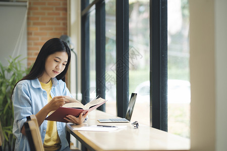 年轻的亚洲女人坐着看书学校文学大学专注项目青少年思维电脑学生图书馆背景图片