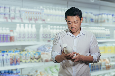 低温酸奶在奶制品部一家超市的亚洲买家 人选择牛奶读标签背景
