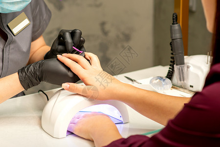 行业沙龙专业美甲 一位美甲师正在一家美容院用紫色指甲油为客户的女性指甲上色 特写 美容行业概念刷子搪瓷女孩抛光手套治疗紫外线工具手指凝胶背景