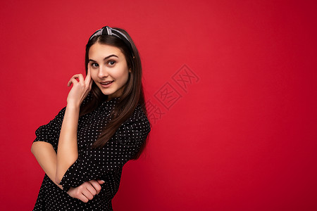 年轻可爱 迷人 美丽 快乐 微笑的黑发女士 带着真诚的情感 身穿黑色衬衫 点缀在红色背景中 空荡荡的背景图片