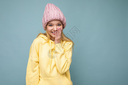 迷人的微笑快乐的金发年轻女性孤立地站在色彩缤纷的背景墙上 穿着日常时尚的服装 看着镜头时表现出面部情绪黄色帽衫可用粉红色蓝色衣服背景