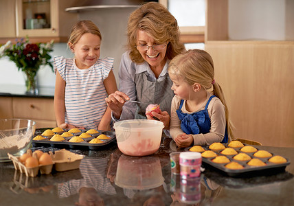 教她的孙子宝贵的厨房技能 两个小女孩在祖母的帮助下在家里烤纸杯蛋糕背景图片