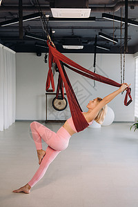 一位身为空中瑜伽教练的少女 正吊在瑜伽会馆大厅的吊床上 一位身穿粉色运动服的女士正在做反重力瑜伽有氧运动冥想衣服女孩运动重力运动背景图片