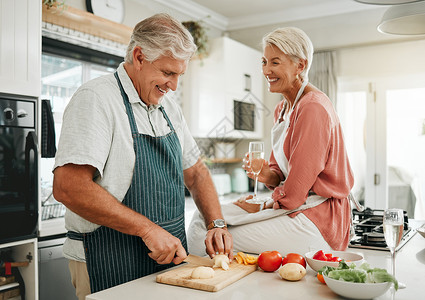 他们都恋爱啦一对幸福的老年夫妇 在厨房里做健康的食物 喝香槟 享受退休生活 坐在柜台上的老妇人 银发男子笑着 他们相爱地微笑背景