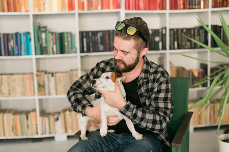 我有责任杰克罗素梗犬的快乐男主人 站在书架背景下 感到有责任照顾宠物 人与动物的关系公寓猎犬成人女性晴天感情男性友谊朋友小狗背景