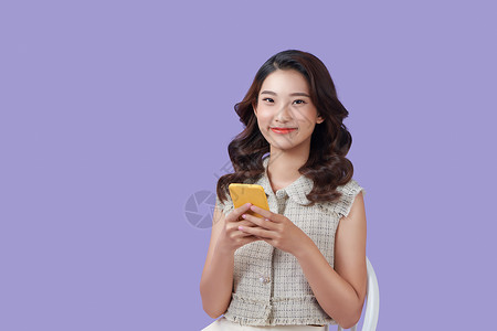 坐在沙发上的亚裔妇女用她的电话 带着快乐的表情成人访问手机乐趣女性微笑互联网女士椅子面试背景图片