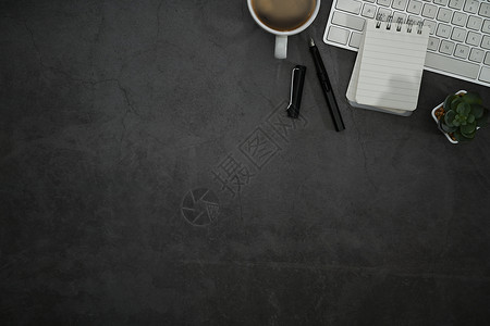 黑色石桌上配有记事本 咖啡杯和无线键盘的时尚工作场所 带复制空间的顶视图背景图片