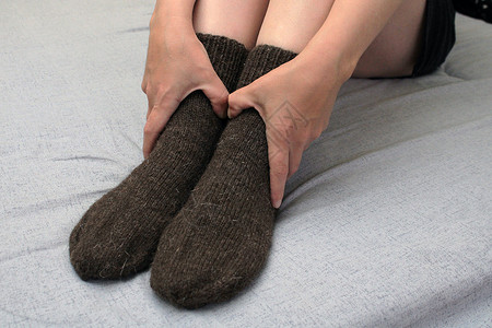 长简袜子素材一位长着苗条双腿的年轻女子穿着棕色羊毛袜坐在家里的床上 世界能源危机的概念衣服加热袜子羊毛房间房子床单织物气体短袜背景