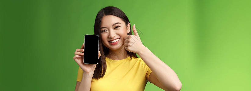 推荐好物特写满足可爱的亚洲女孩给予积极反馈 竖起大拇指显示智能手机屏幕 介绍很棒的新应用程序 推荐好的应用程序 在游戏中吹牛打分旅游女朋背景