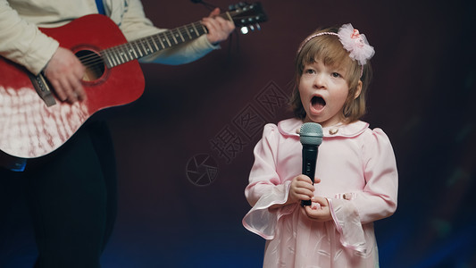穿旧礼服的小女孩在舞台上唱歌 她父亲弹声吉他戏服爱好才俊爸爸连衣裙衣服幼儿园国家舞蹈岩石背景图片