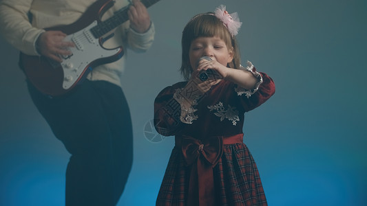 幼儿园秀素材穿旧礼服的小女孩在舞台上唱歌 她父亲弹电吉他嗓音复古油烟机幼儿园彩色音乐家庭背景蕾丝戏服背景