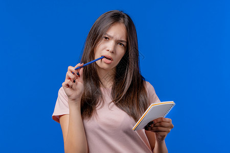 年轻女子用笔在规划师中写笔记 女学生在笔记本虑周 月 年的未来计划和待办事项列表 在蓝色背景上保留个人日记背景图片