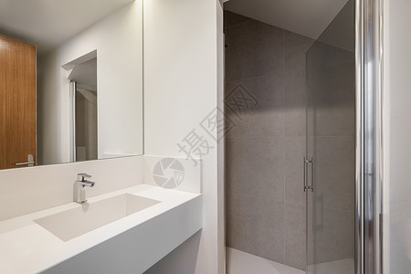 浴室玻璃门敞开的玻璃门从浴室通向带有灰色瓷砖墙和白色瓷砖地板的淋浴区 浴室配有带金属水龙头和大镜子的白色卫生洁具水槽背景