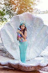 美人鱼公主一个微笑的小女孩 穿着美人鱼服装 在大贝壳 拿着一个多彩的海马玩具戏服舞蹈家孩子警笛情调女孩头发手势黑发海滩背景