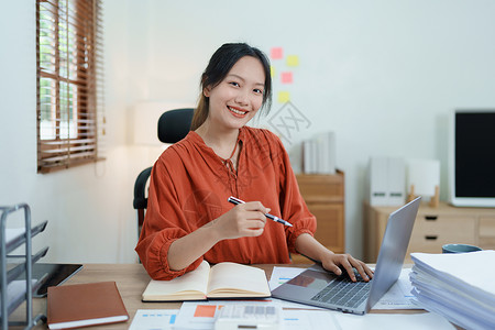 一位女企业主的画像 她在工作中使用电脑和财务预算文件成功地投资了她的企业时 脸上挂着快乐的笑脸商务摄影会议员工手臂衬衫幸福簿记经背景