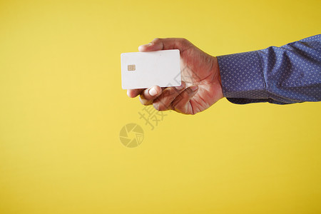 以黄色背景持有信用卡的手持信用卡者;背景图片